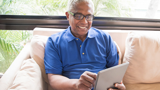 African-American senior man sitting on couch reading a tablet computer