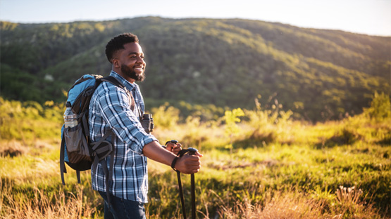 A person smiles while hiking through a grassy, hilly area.