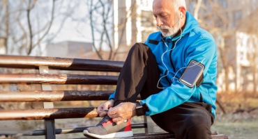 adult senior male tying his shoes on a park bench 