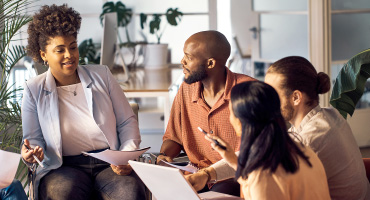 four people in an office meeting talking about employee health benefit trends