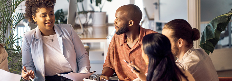 four people in an office meeting talking about employee health benefit trends