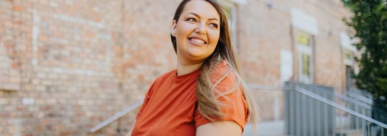 A woman smiling wearing an orange shirt and looking over her shoulder.