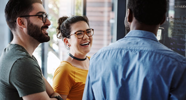 Three people work together in an office, as two smile and listen to the third person.