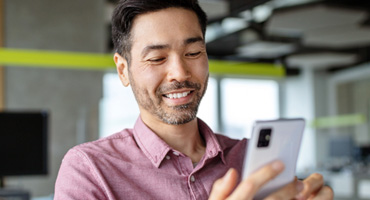 a happy adult smiles while looking at a cell phone in an office setting