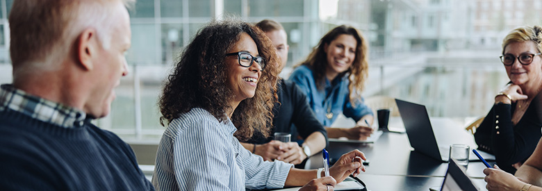 A diverse group of professionals smiling and collaborating around a conference table in a modern office.