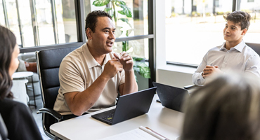Man sitting in a chair with laptop talking to a group