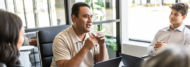 Man sitting with his laptop in an office chair talking to group.