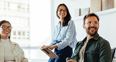 Two women and a man smiling colleagues in an office setting.