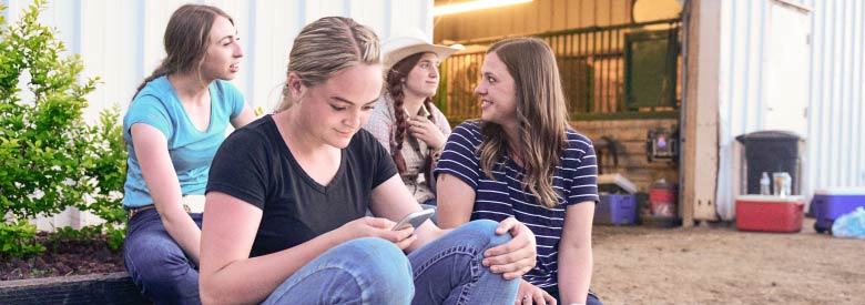 a young girl on her mobile device searching her health insurance provider while with a group of friends