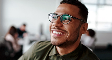 smiling man in an office setting with a table of coworkers in the background