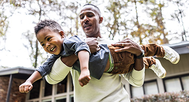neA happy man holds two young children, one of whom is smiling brightly.ed