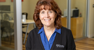 A HIghmark Direct Medicare agent smiles in front of an office with glass walls and a Highmark Direct logo is on their cardigan.