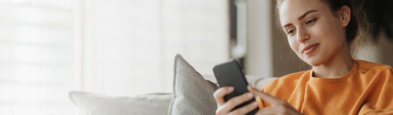 smiling young women sitting on sofa reading her phone smiling