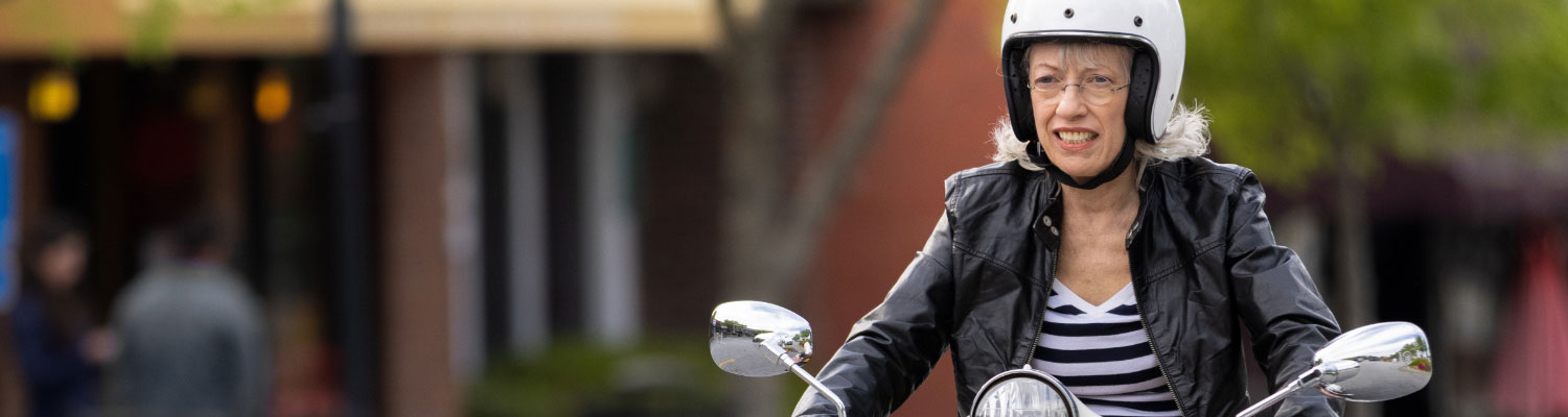 older woman riding scooter wearing a helmet with striped shirt and leather jacket