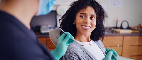 woman smiling, sitting in a dentist chair looking at a dental hygenist about to start her exam