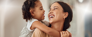 A happy adult embracing a child from behind, both smiling. This image represents the frequently asked questions section for Highmark Healthy Kids.