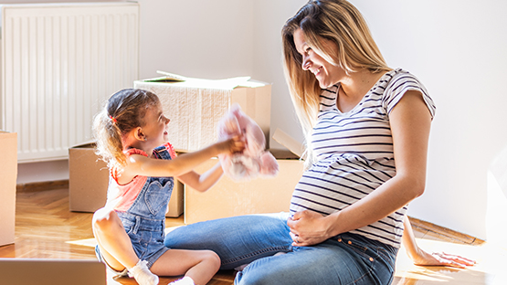 A pregnant parent is sitting on the floor with their child, who is giving them a stuffed animal.