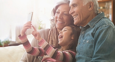 Grandparents with grandchild on their lap, all smiling. Child takes a selfie of group covered by Highmark Medicare Plans.