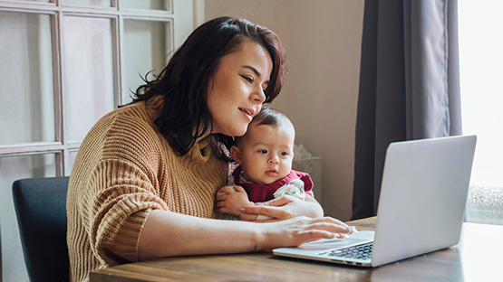 women on her laptop computer while holding a baby seaching spending account options
