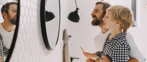 father and son brushing teeth in bathroom smiling in front of mirror