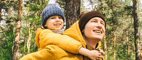 man with young son on his back outside in the woods
