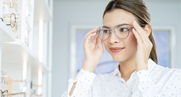 An adult smiles while trying on glasses in an eye doctor's office.